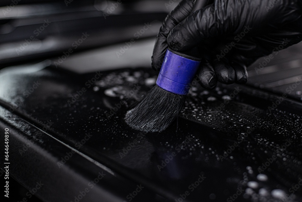 Car wash employee or auto detailing student cleans the engine cover in