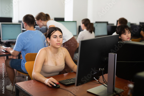 Concentrated Latin female student using PC and studying computer science in the classroom.