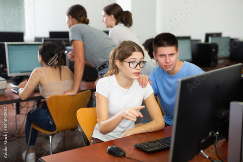 Smart male teenager giving a clue to the female co-learner while she is using pc in the computer classrooms