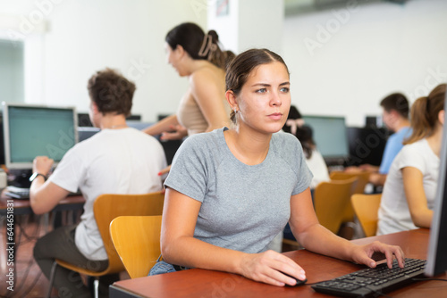 Girl preparing for exam in college library, using pc for searching information