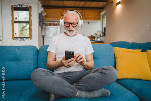 one senior man with headphones use smsrtphone to play music at home