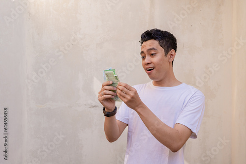 Indonesian men happy and smile when hold the money wear white tshirt. The photo is suitable to use for man expression advertising and fashion life style.