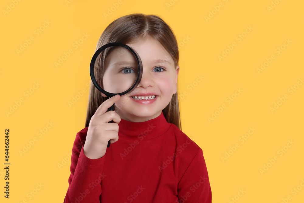Cute little girl looking through magnifier on yellow background Cute little girl looking through magnifier on yellow background