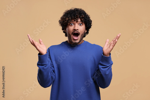 Handsome surprised man on beige background. Space for text