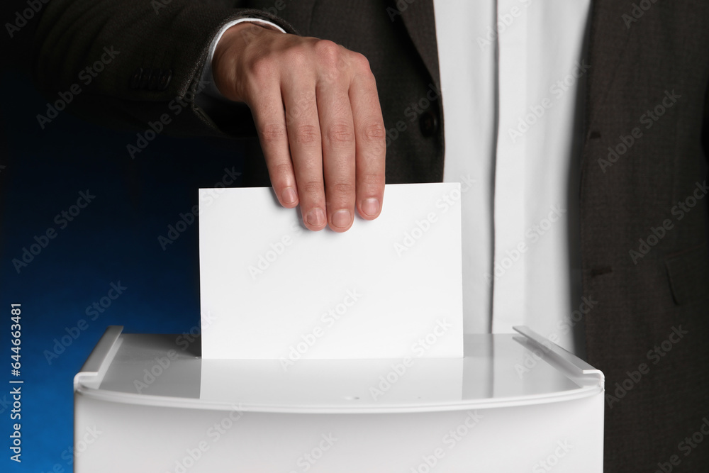 Man putting his vote into ballot box on dark blue background, closeup Man putting his vote into ballot box on dark blue background, closeup