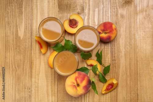 Glasses of peach juice, fresh fruits and leaves on wooden table, flat lay