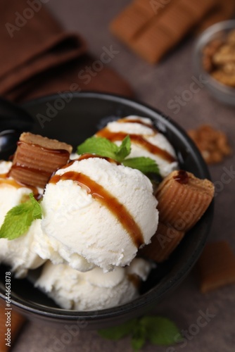 Bowl of tasty ice cream with caramel sauce, candies and mint on brown table, closeup