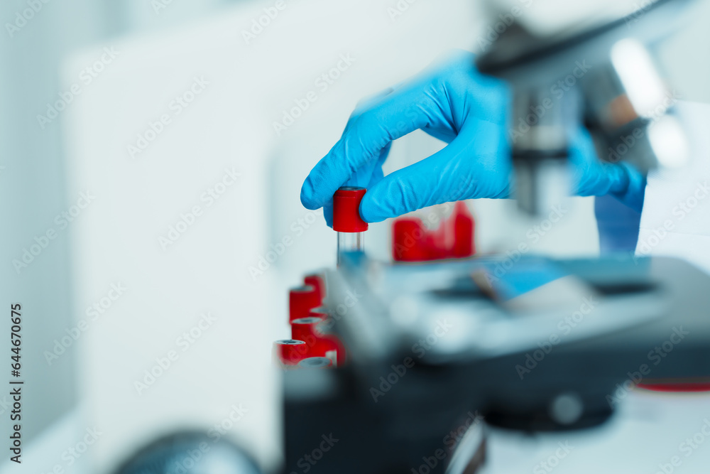 Close up dedicated hematology lab technician scrutinizing blood sample analysis under microscope, scientific laboratory research and drug testing concept, red color liquid