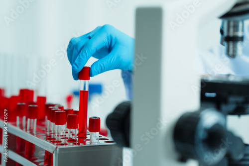 Close up dedicated hematology lab technician scrutinizing blood sample analysis under microscope, scientific laboratory research and drug testing concept, red color liquid