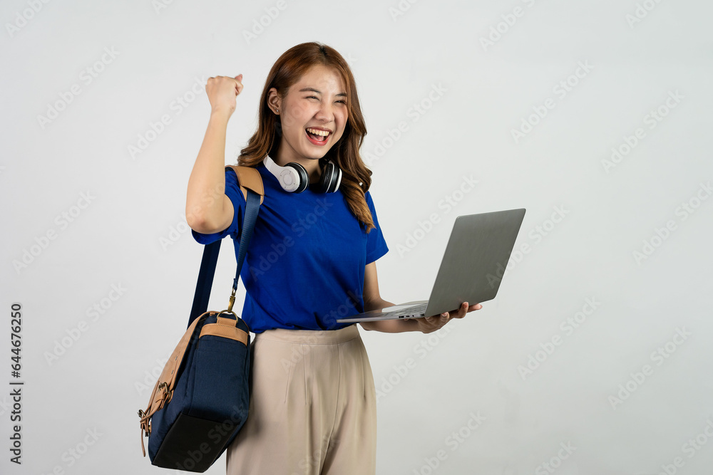 Happy young Asian female student with backpack standing and holding laptop. Woman in blue t-shirt working on laptop computer isolated on white background. Online education concept. Happy young Asian female student with backpack standing and holding laptop. Woman in blue t-shirt working on laptop computer isolated on white background. Online education concept.