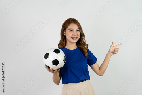 Happy Asian female soccer fan sending support to favorite team with soccer ball, smiling woman in blue t-shirt holding soccer ball to cheer at soccer game, isolated on white background. © ArLawKa