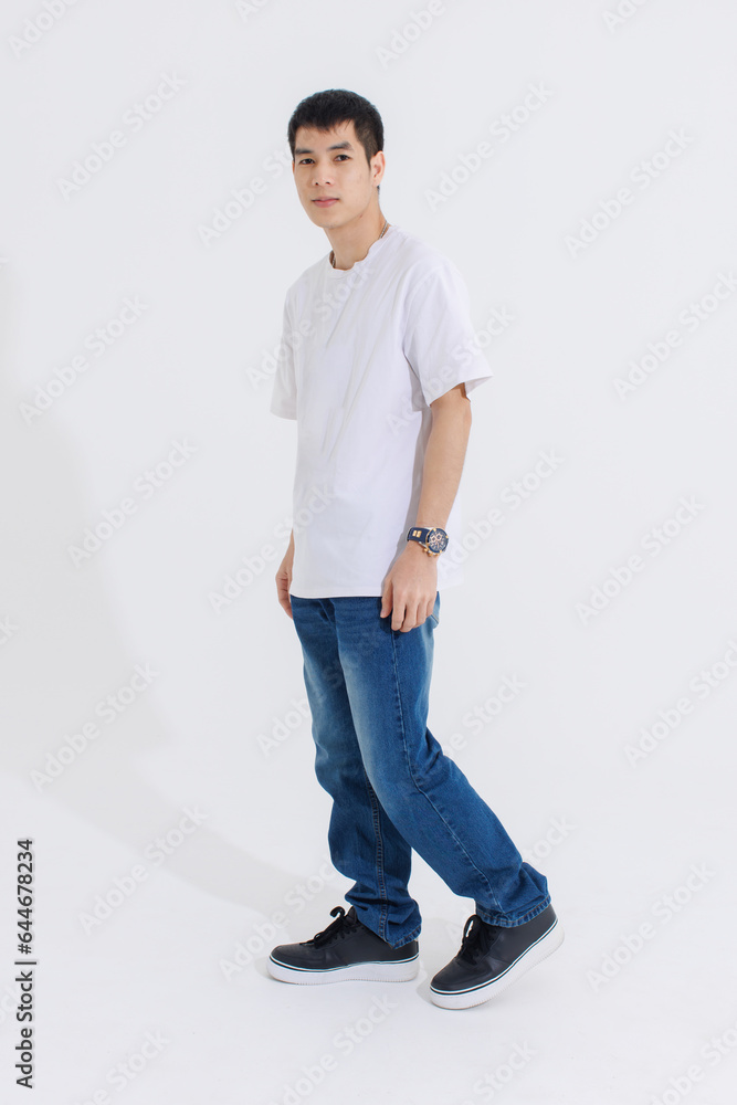 Portrait isolated cutout studio full body shot Asian handsome cool male fashion model in casual fashionable t shirt and blue jeans standing holding hands in pockets look at camera on white background Portrait isolated cutout studio full body shot Asian handsome cool male fashion model in casual fashionable t shirt and blue jeans standing holding hands in pockets look at camera on white background