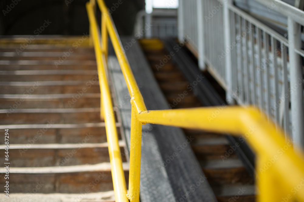 Steep stairs. Yellow handrail for climbing stairs. Overhead road crossing.