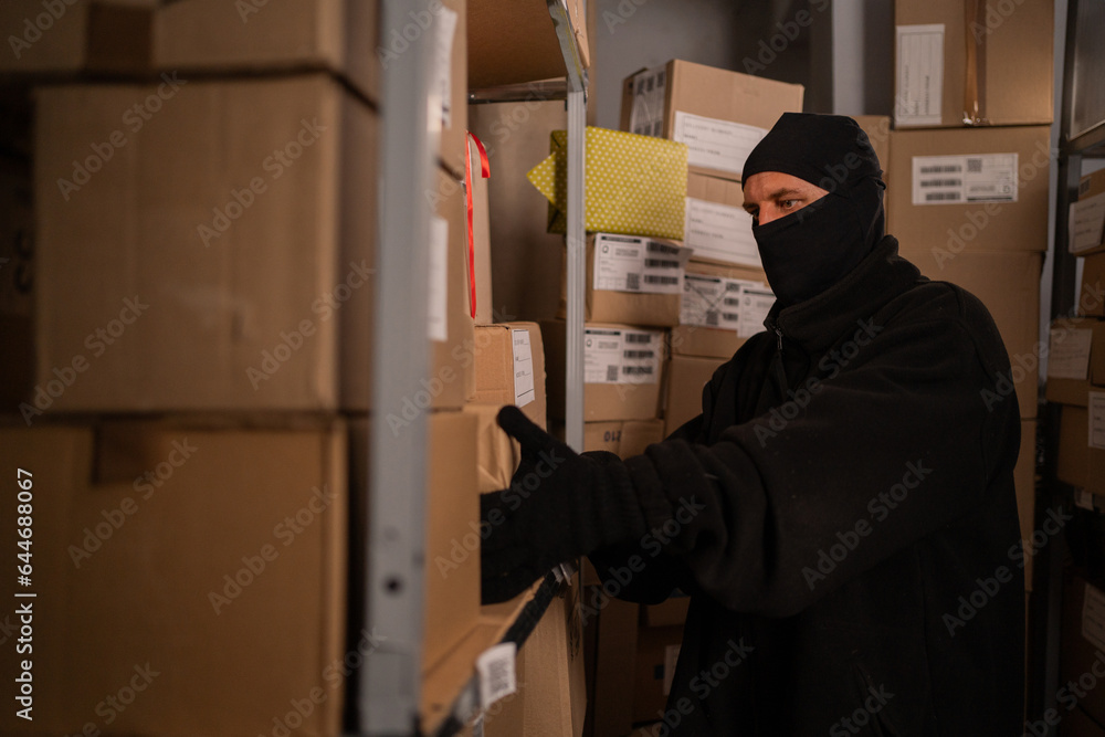Thief in black gloves take a boxes of goods in a warehouse at night. Security problems in warehouses and stores. Thief in black gloves take a boxes of goods in a warehouse at night. Security problems in warehouses and stores.
