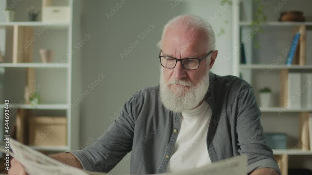 A Serious, Smart Old Man Sits at a Table and Reads a Newspaper.An Elderly Man with a Newspaper Alone at Home, Sees the News and Current Events in the Newspaper.Daily Newspaper Concept A Serious, Smart Old Man Sits at a Table and Reads a Newspaper.An Elderly Man with a Newspaper Alone at Home, Sees the News and Current Events in the Newspaper.Daily Newspaper Concept