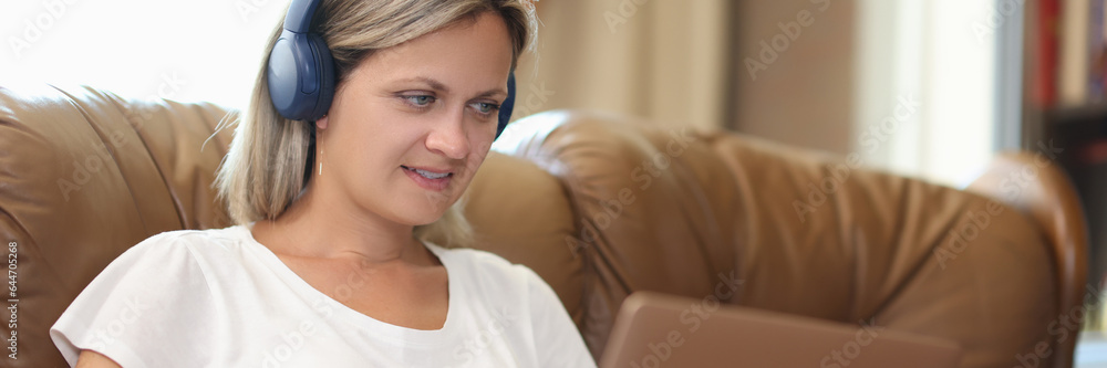 Naklejka premium Smiling woman in headphones working on laptop at home