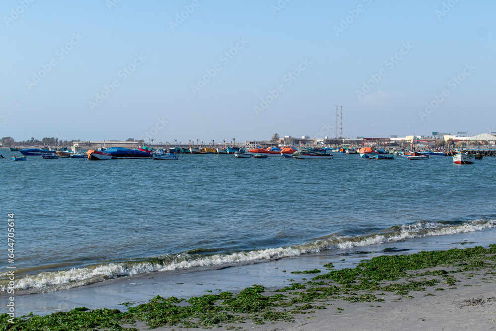 Muelle en la Mar con botes y personas a la orilla de la playa