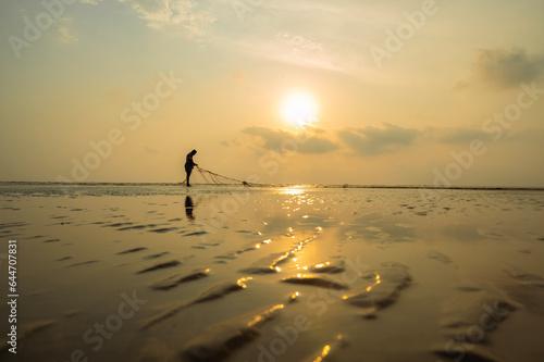 Photo shot of a fisherman while fix his fishing net on the sea beach at sunset time. 03.28.2023. Bakkhali, South 24 Parganas, West bengal, India.