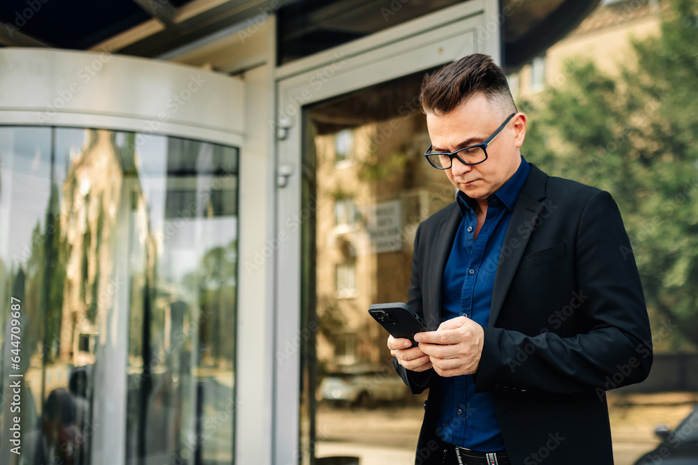 Fototapeta premium Closeup happy handsome male businessman successful on the city street. Portrait of a successful man outdoors. Modern gadgets for lifestyle.