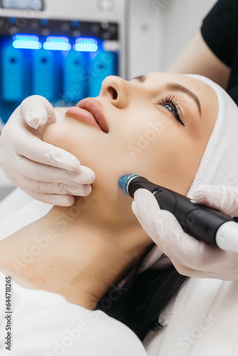 View of doctor cosmetologist doing anti aging procedure in cosmetology office. Satisfied woman in disposable hat lying on couch and relaxing. Working with Apparatus. photo