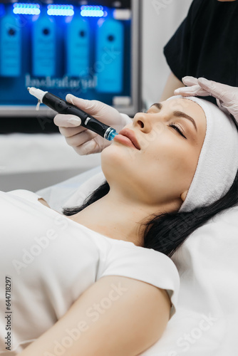 Professional dermatologist in medical gloves doing hydro peeling procedure for beautiful woman patient in cosmetology clinic. Close up facial treatment.