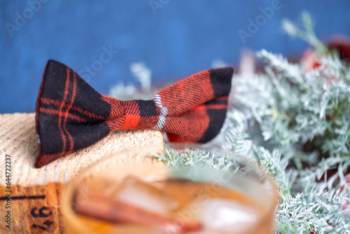 Red black checkered bow on a wooden pad and juniper branch in the background. Glass of drink in foeground. Lumperjack Christmas mood. Copy space photo