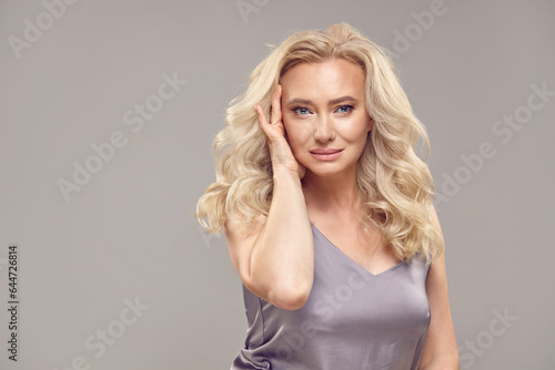 Beauty blonde senior woman with a curly blonde hair and healthy skin on a grey isolated © Ilshat