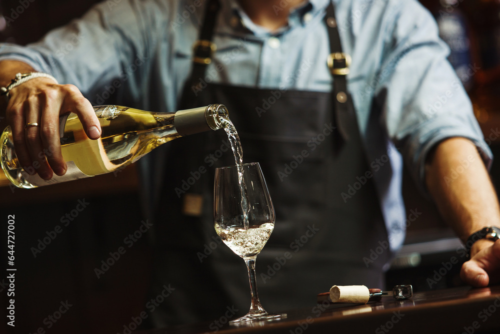 Fototapeta premium Male sommelier pouring white wine into long-stemmed wineglasses.