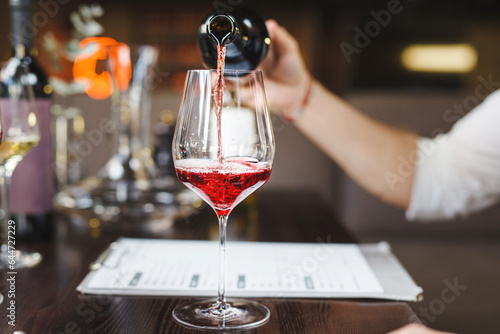 Photo Faceless sommelier pours red wine into stem glass.