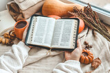 Open Bible in female hands in autumn interior