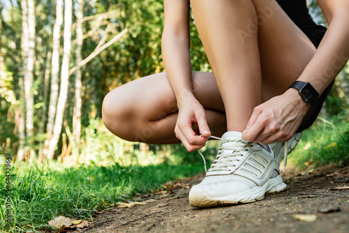 Fototapeta Naklejka Na Ścianę i Meble -  A female runner ties white sneakers before jogging in a summer forest.