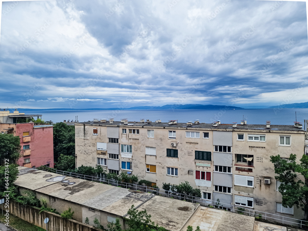 Old houses in front of the Adriatic Sea or Mediterranean Sea in Rijeka in Croatia, with mountains and clouds in the background 