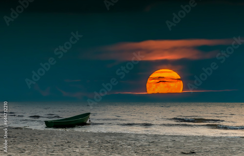 Coastal landscape during colorful rise of super-moon above cloudy horizon wit...