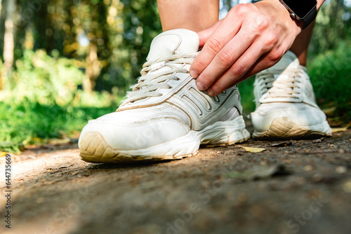 Close up of female runner ties white sneakers before jogging in a summer forest.