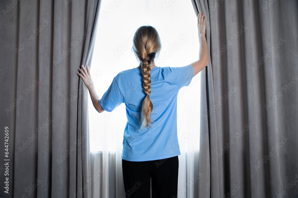Girl at home opens the curtains and looks out the window