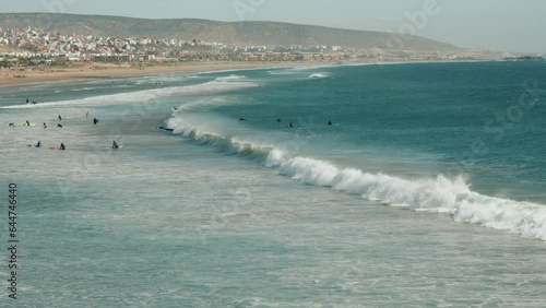 Wide view of a beach, shore and people surfing on sea waves in Agadir, Morocco. photo