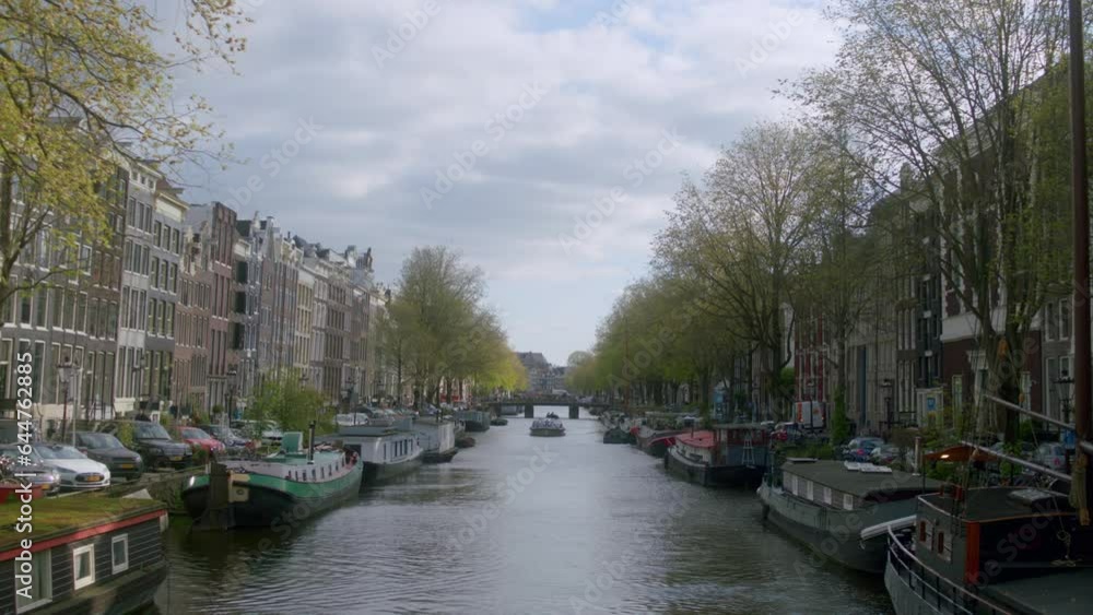 Iconic Canal Boats Moored Near The Port And Typical Building Architecture In Amsterdam, Netherlands. static, wide shot Iconic Canal Boats Moored Near The Port And Typical Building Architecture In Amsterdam, Netherlands. static, wide shot