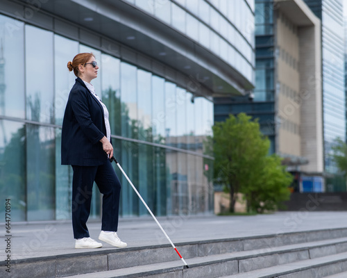 Blind business woman descending stairs with a tactile cane from a business center.