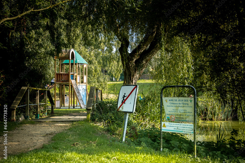 Photographie d'une aire de jeux près d'un étang et de leurs signalétiques. Photographie d'une aire de jeux près d'un étang et de leurs signalétiques.