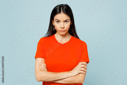 Young frowning sad latin woman wearing orange red t-shirt casual clothes hold hands crossed folded look camera isolated on plain pastel light blue cyan background studio portrait. Lifestyle concept. photo