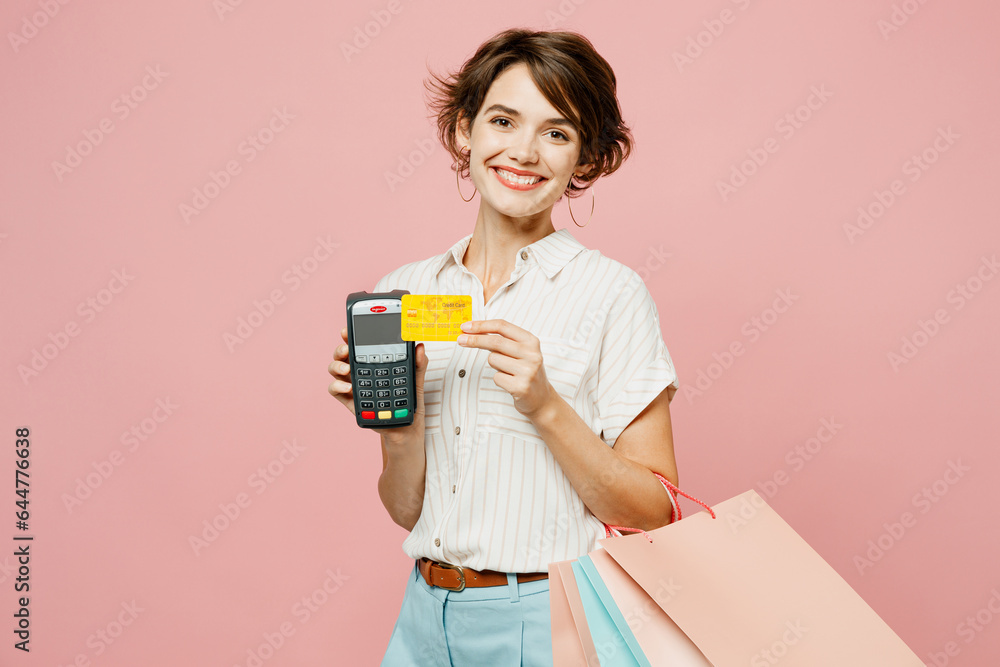 Young woman wear casual clothes hold shopping paper package bags wireless bank payment terminal process acquire credit card isolated on plain pink color background Black Friday sale buy day concept.