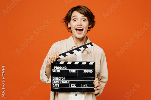 Young excited happy caucasian woman she wear beige shirt casual clothes hold in hand classic black film making clapperboard isolated on plain orange red background studio portrait. Lifestyle concept. photo
