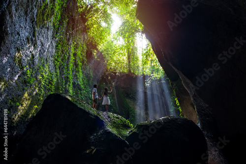 Young couple tourism with rays of light enjoying Tukad Cepung Waterfall at Bali, Indonesia