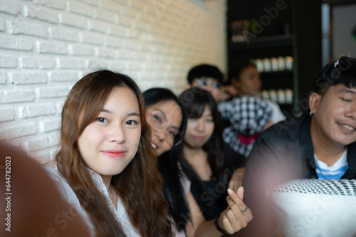 Group of asian friends sitting on sofa in cafe and taking selfie with smartphone