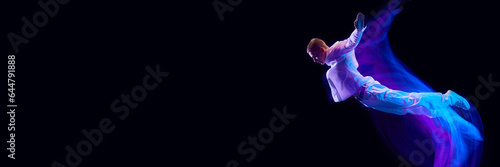 Freedom. Young guy in stylish clothes falling down over black studio background in neon with mixed lights effect. Concept of movements, art, dance and sport, fashion, youth. Banner. Copy space for ad