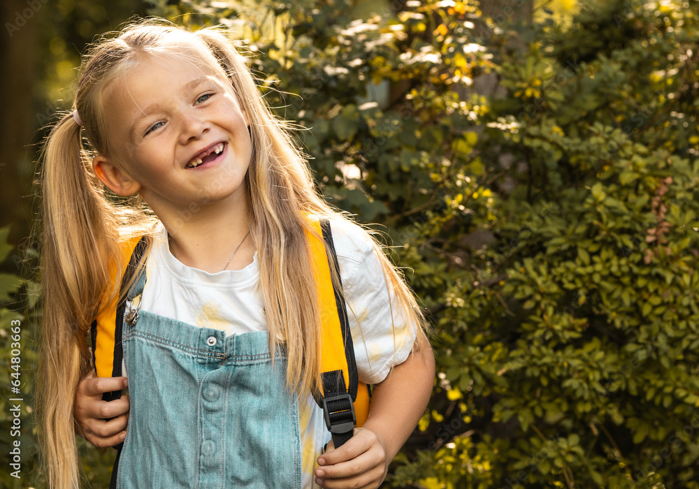 Grade R Portrait Cute smiling little girl with backpack on a greenery background ...
