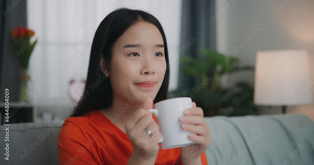 Asian woman drinking a coffee while sitting on the sofa Asian woman drinking a coffee while sitting on the sofa