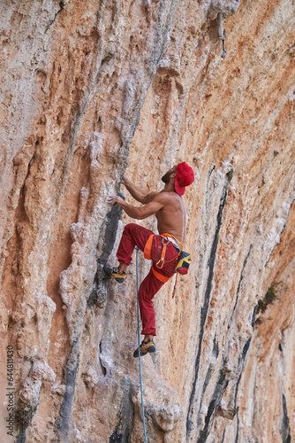 Muscular man climbing rocky cliff