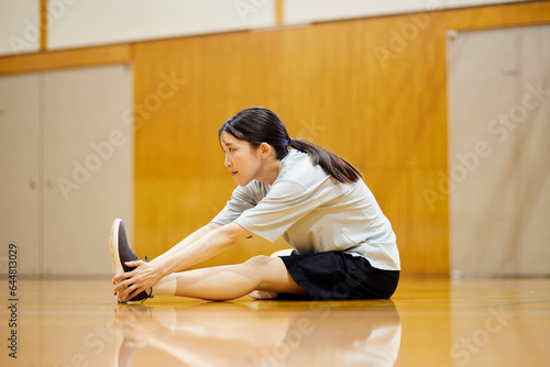 体育館にてストレッチを行うスポーツウェアを着た日本人女性