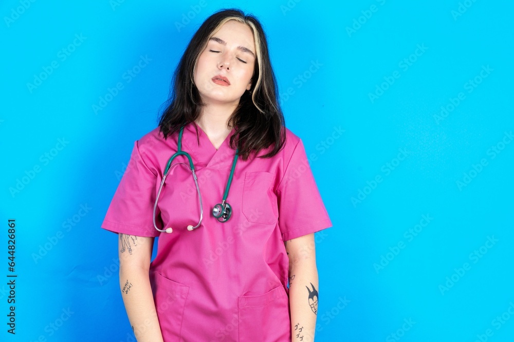 Young caucasian doctor woman wearing pink medical uniform looking sleepy and tired, exhausted for fatigue and hangover, lazy eyes in the morning. Young caucasian doctor woman wearing pink medical uniform looking sleepy and tired, exhausted for fatigue and hangover, lazy eyes in the morning.